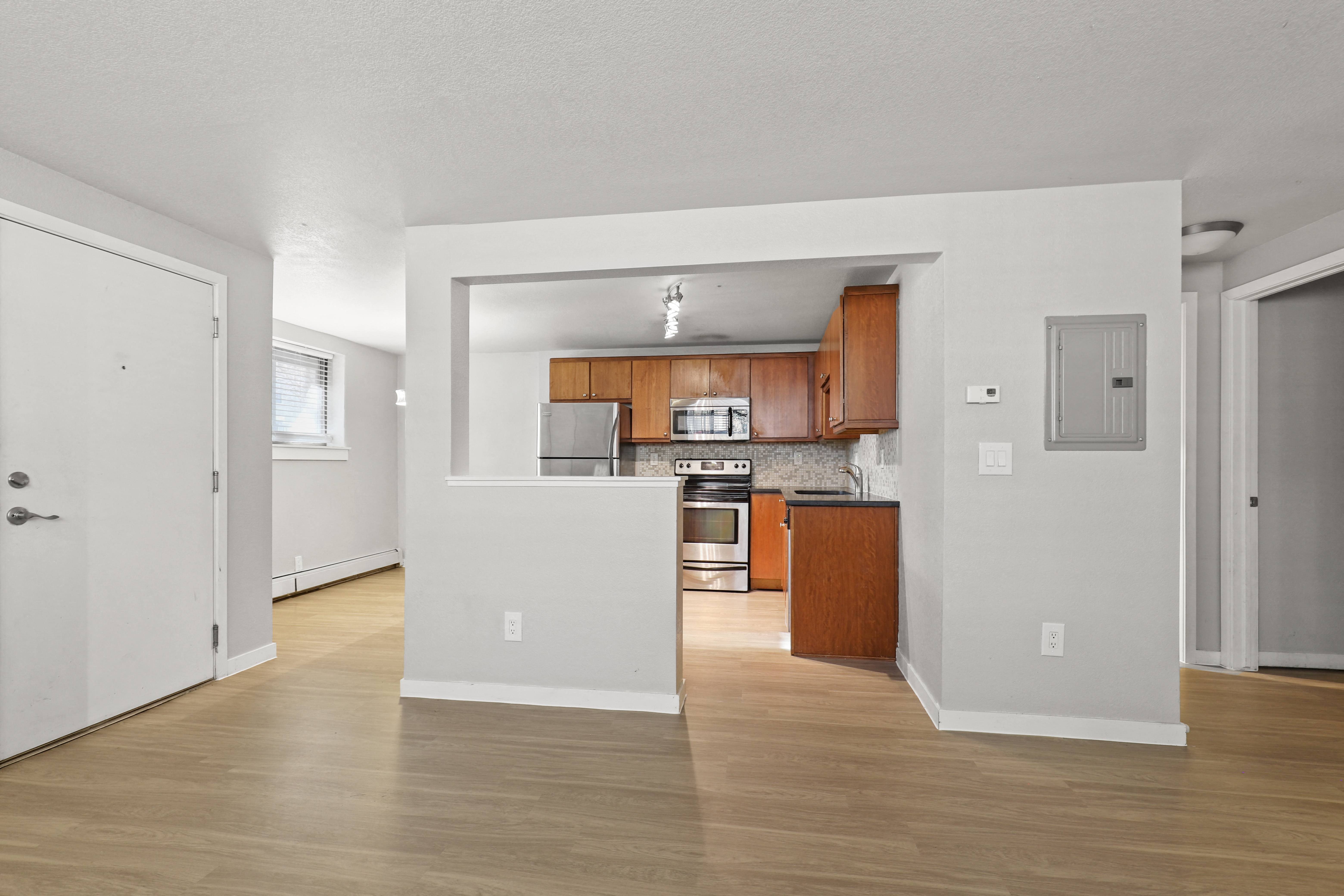 an empty living room and kitchen with wood flooring and white walls